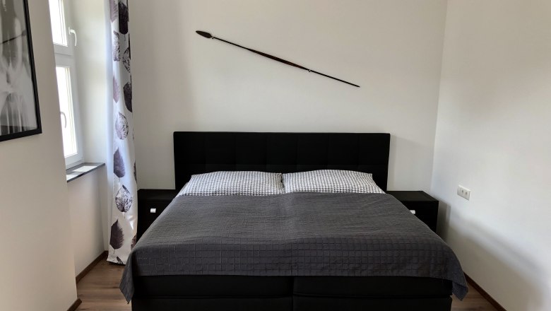 Modern bedroom with a large bed, gray comforter and a spear on the wall.