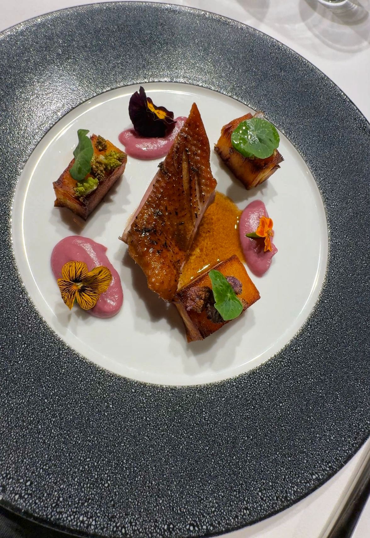Gourmet dish with duck breast, diced vegetables and flowers on an elegant plate.