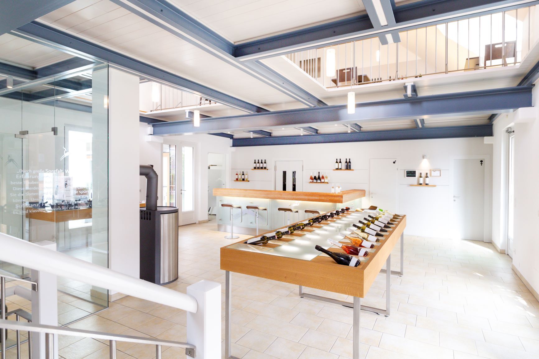 Interior view of a modern wine shop with wine bottles on a table and a bar in the background.