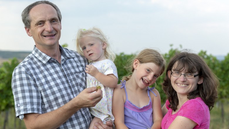 A family stands smiling in a vineyard.