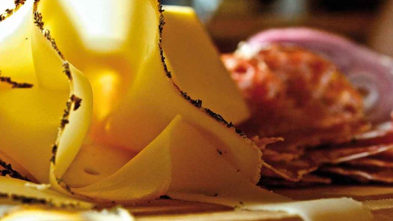 Close-up of thinly sliced cheese and sausage on a wooden board.