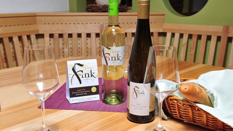 Two bottles of wine and glasses on a wooden table with a bread basket.