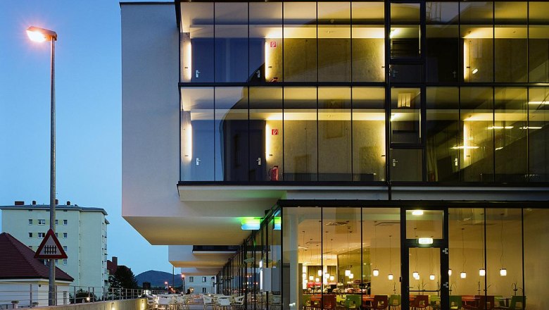 Modern hotel building with glass façade at dusk, illuminated interiors visible.