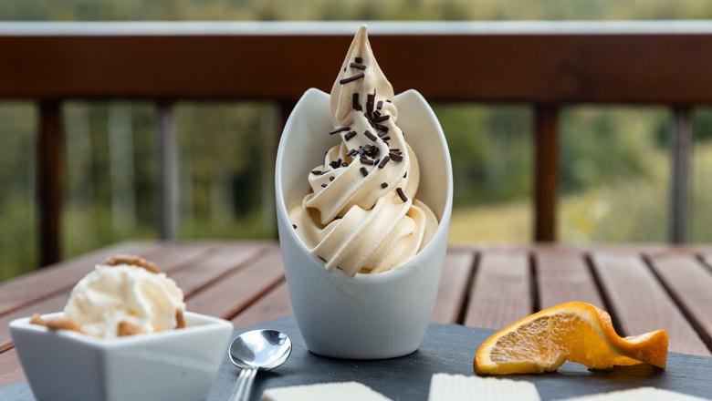 A dessert with soft ice cream, chocolate sprinkles, waffles and an orange slice on a table.