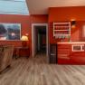 Interior view of a modern living room with red walls, a red kitchenette, brown armchairs and a large window.