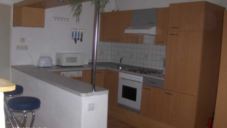 Modern kitchen with wooden cupboards, bar stools and appliances such as microwave and stove.