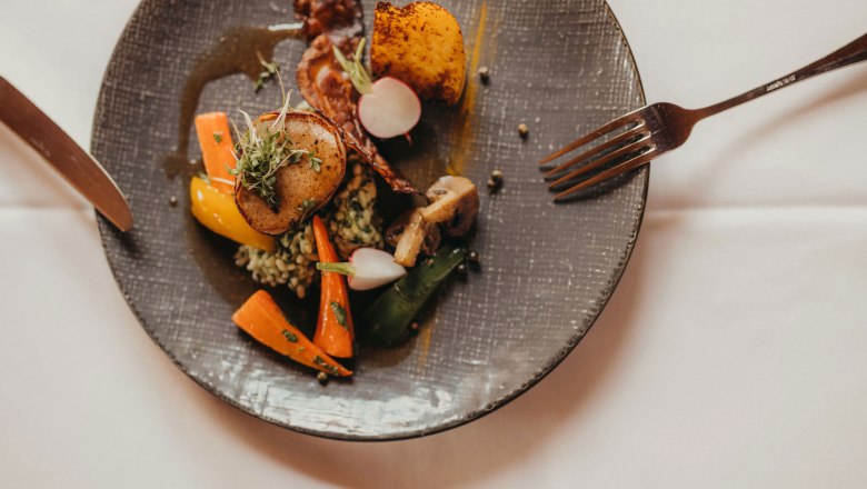 A plate of pork fillet wrapped in bacon, wild garlic risotto, vegetables and potatoes.