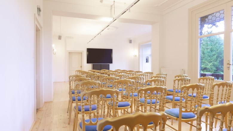 A bright lounge with rows of chairs and a large screen on the wall.