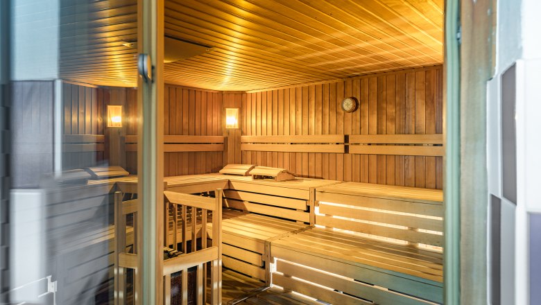 Interior view of an empty sauna with wooden benches and wall clock.