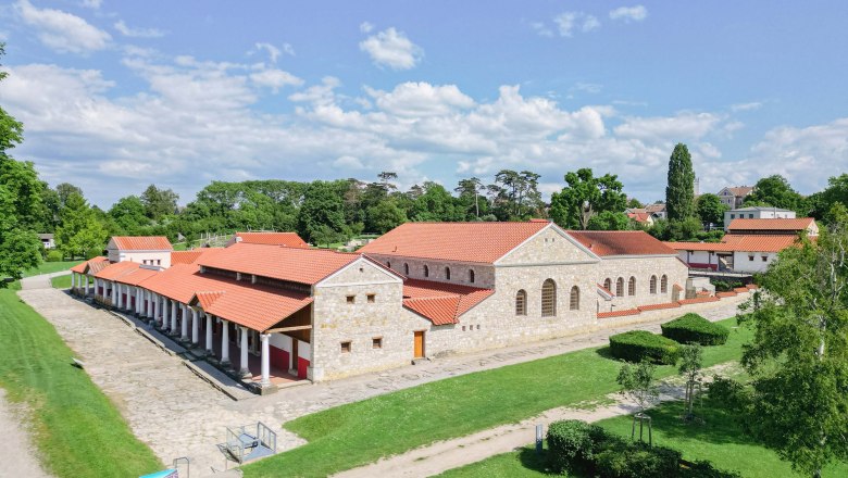 Roman town of Carnuntum with reconstructed buildings and red roofs, surrounded by green trees and lawns.