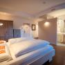 Modern hotel room with double bed, wooden wardrobe and open bathroom.