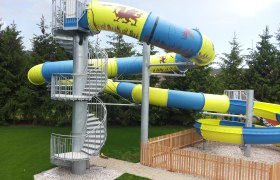 Large water slide with blue and yellow tubes and spiral staircase.