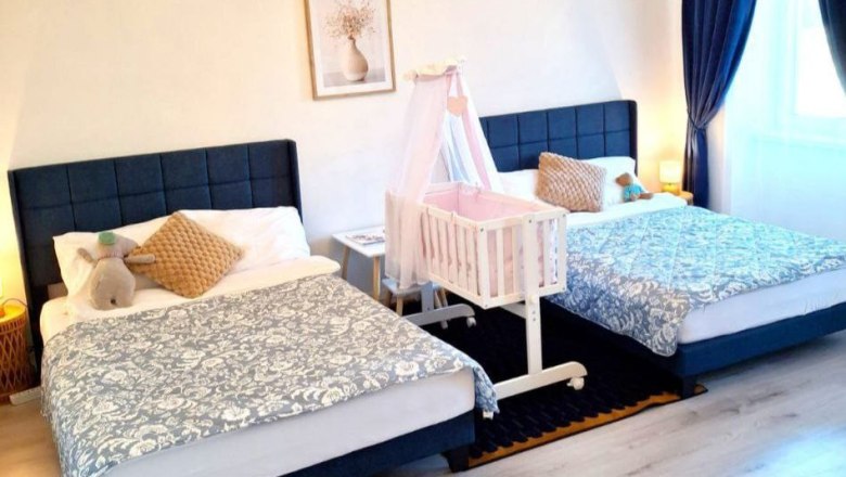 One bedroom with two double beds, a baby crib in the middle and blue curtains.