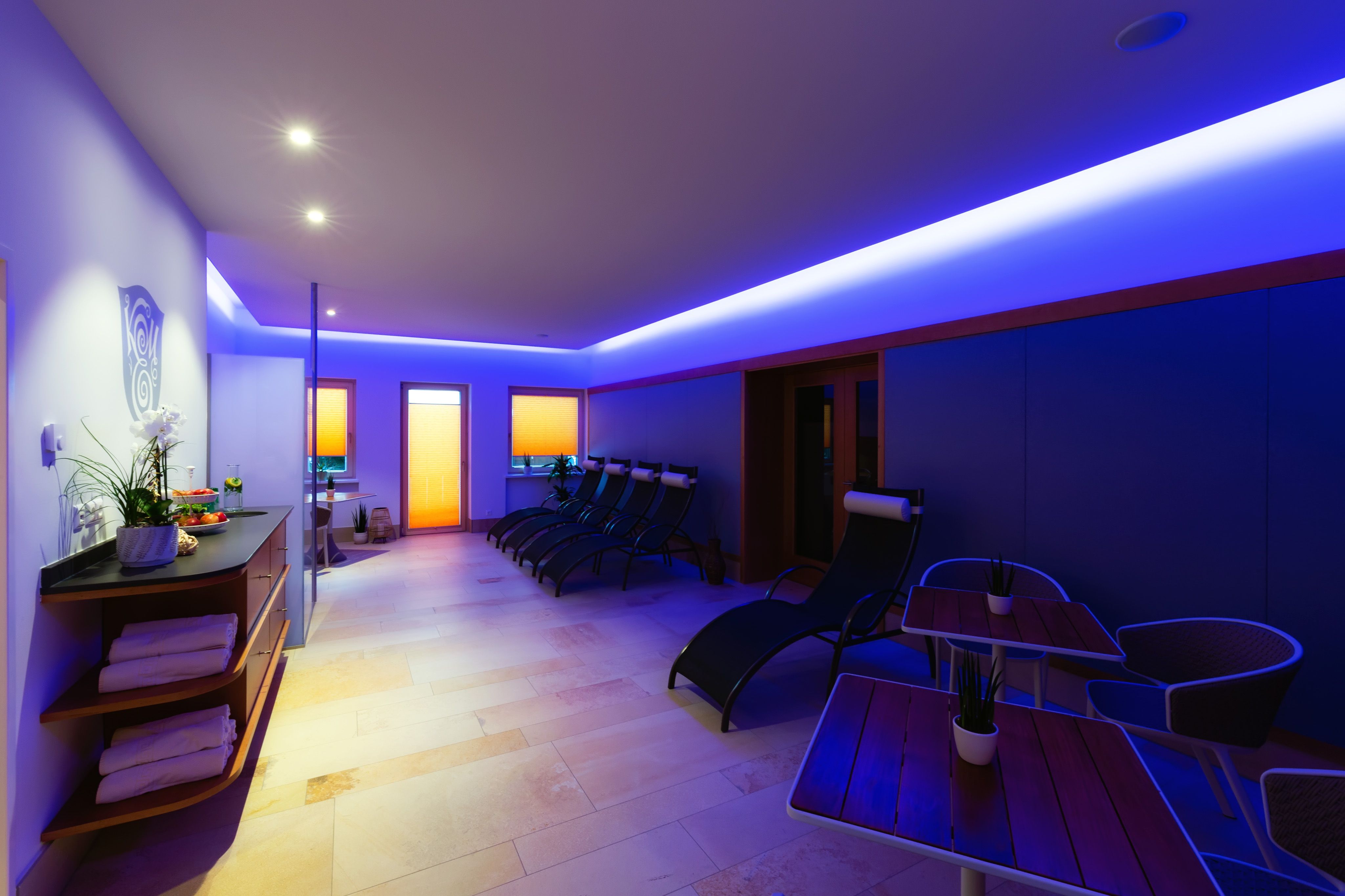 A modern wellness area with loungers, tables and blue lighting.