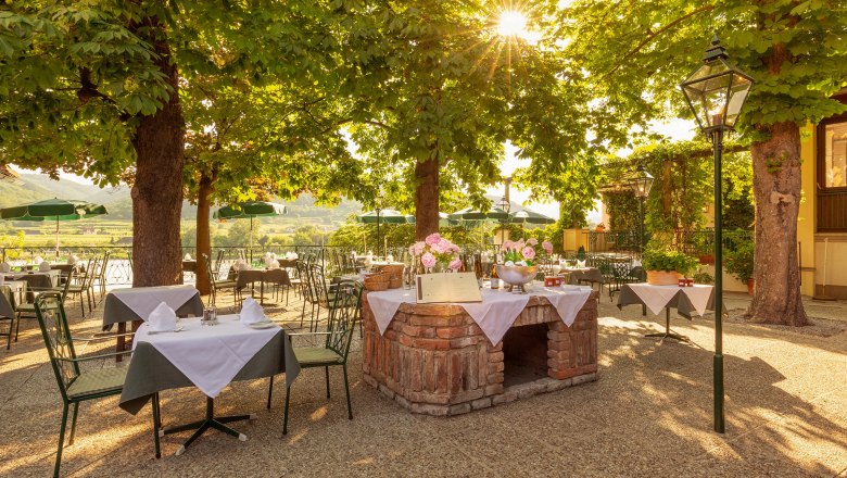 A sunny outdoor area of a restaurant with covered tables under trees.