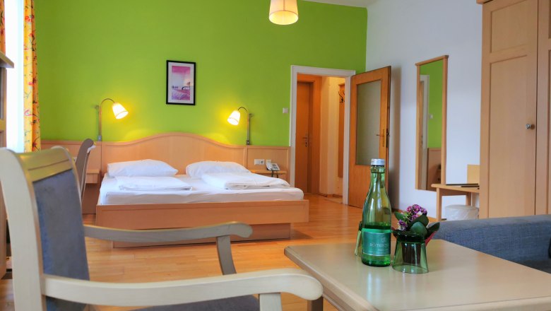 A cozy double room with green-painted wall, double bed, table, chairs and water bottle.