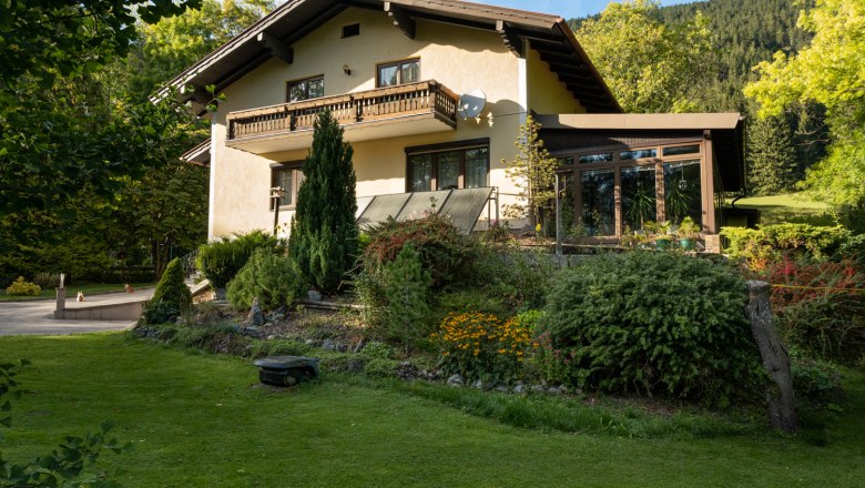 A two-storey vacation home with balcony and garden, surrounded by trees and meadow.