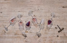 Overturned wine glasses with red wine on a wooden table.
