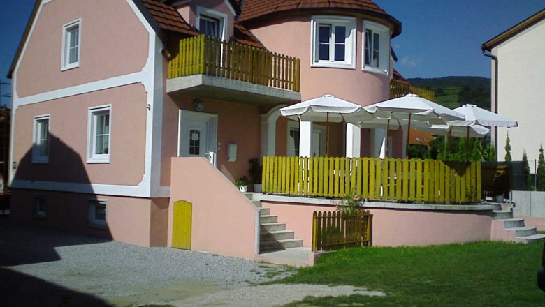 A pink guest house with terrace and parasols.