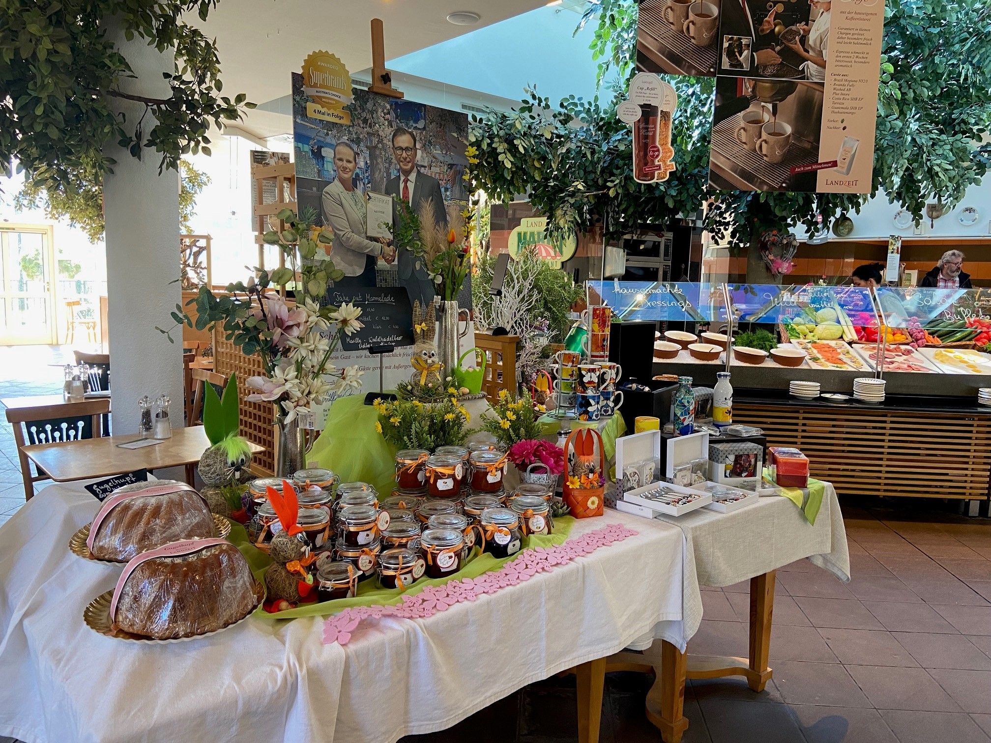 A table with jam jars, cakes and decorations in a restaurant with a buffet in the background.