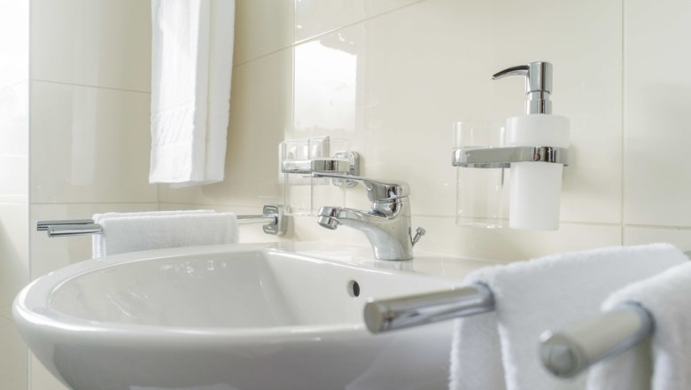 Modern bathroom with washbasin, towels and soap dispenser.