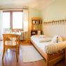 Comfortable twin room with wooden furniture, two beds, table, chairs and a window with curtains.