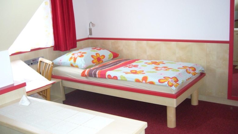 A simple room with a single bed, a desk and a chair. The bed linen has a floral pattern.