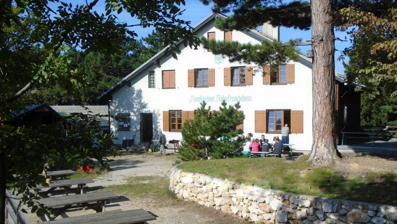A building with the inscription 'Neunkirchner Naturfreundehaus', surrounded by trees and benches outside.