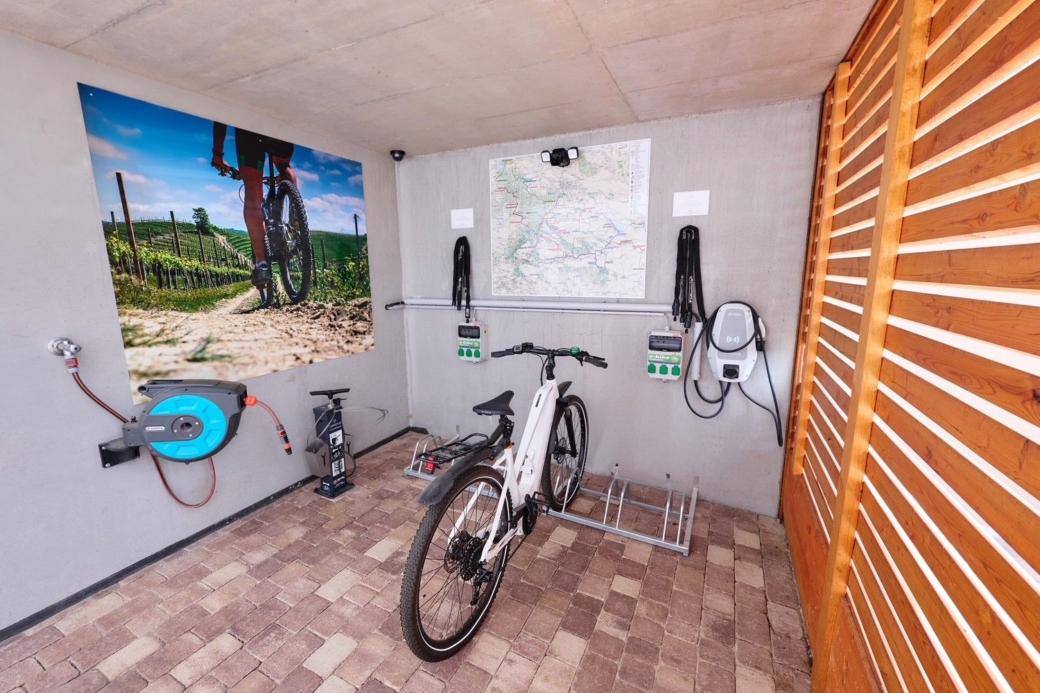 Bicycle in a garage with charging stations and mural of a cyclist in a vineyard.