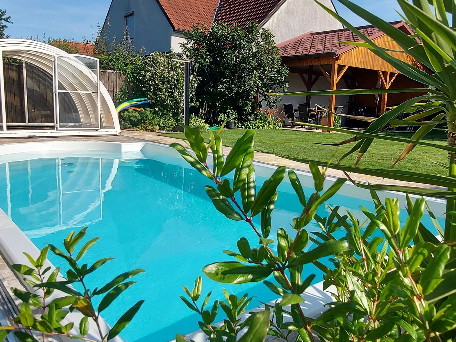 A private garden with a pool surrounded by plants and a covered seating area.