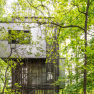Modern tree house in a dense forest, surrounded by green leaves.
