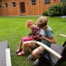 Two children are sitting on deckchairs in the garden, holding small animals in their hands.
