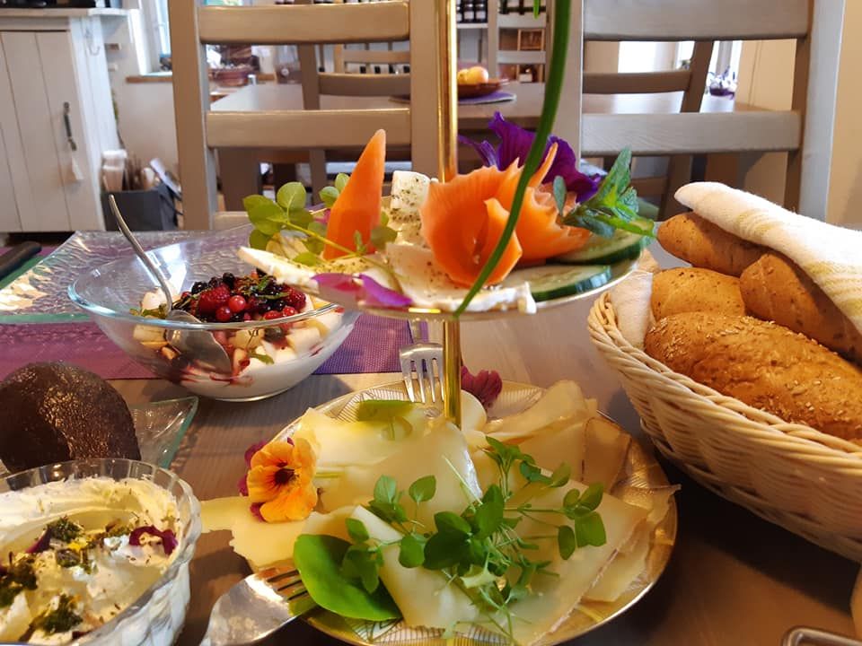 A laid breakfast table with bread rolls, cheese, yogurt with berries and decorative flowers.