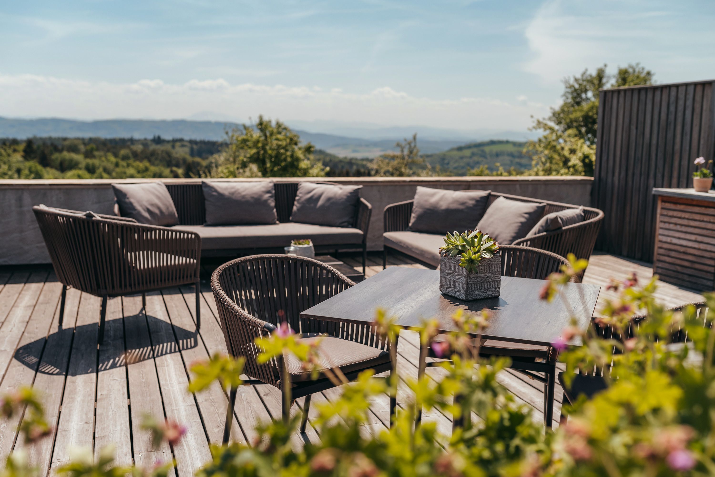 Terrace with seating furniture and plants, with a wide landscape in the background.