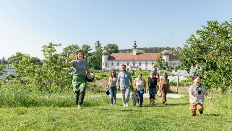 A group of people walk across a meadow, in the background a building with onion domes.