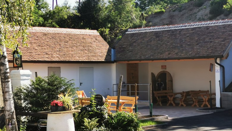 A cozy outdoor area with wooden benches and plants in front of a building with a tiled roof.