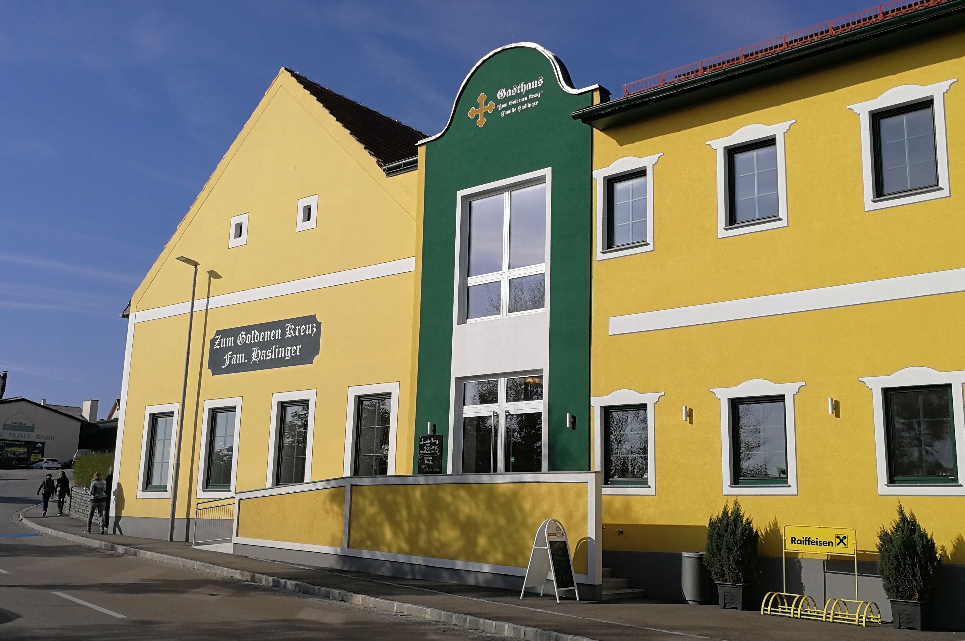 Yellow building with green facade and the inscription 'Zum Goldenen Kreuz Fam. Haslinger'.