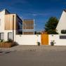 Modern building with a white façade and wooden elements, surrounded by a wall with a wooden gate.