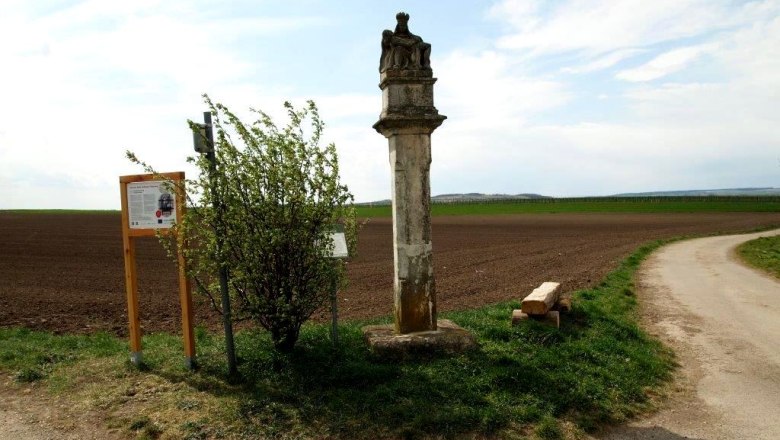 Stone pillar next to a field path with information board and bushes.