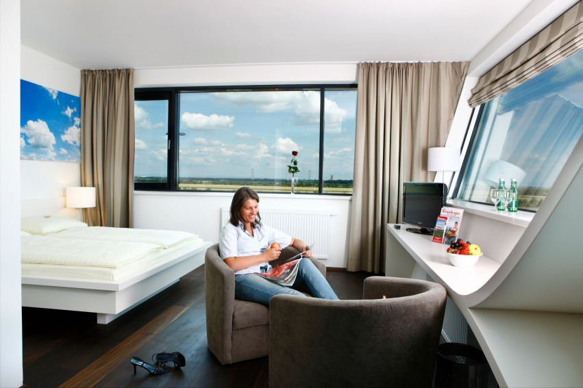 Woman sitting in a modern hotel room with a large window, reading a magazine.