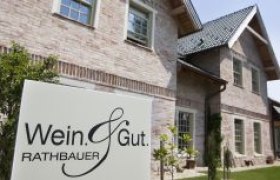 A sign with the inscription 'Wein & Gut Rathbauer' in front of a brick building.