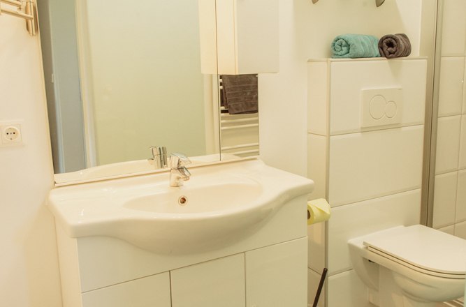 Modern bathroom with washbasin, mirror, toilet and shelves.