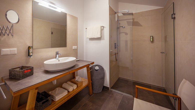 Modern bathroom with washbasin, mirror, shower and towels.