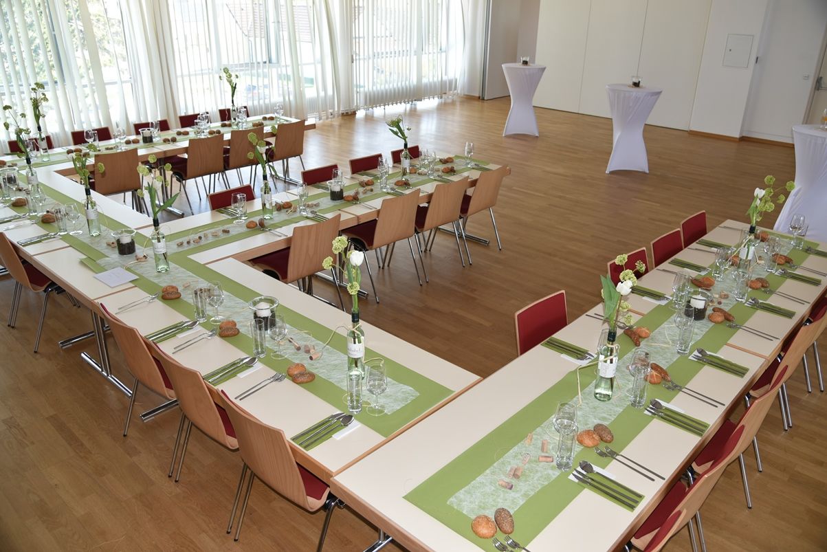 A festively decorated hall with tables arranged in a U-shape, green table runners and floral decorations.