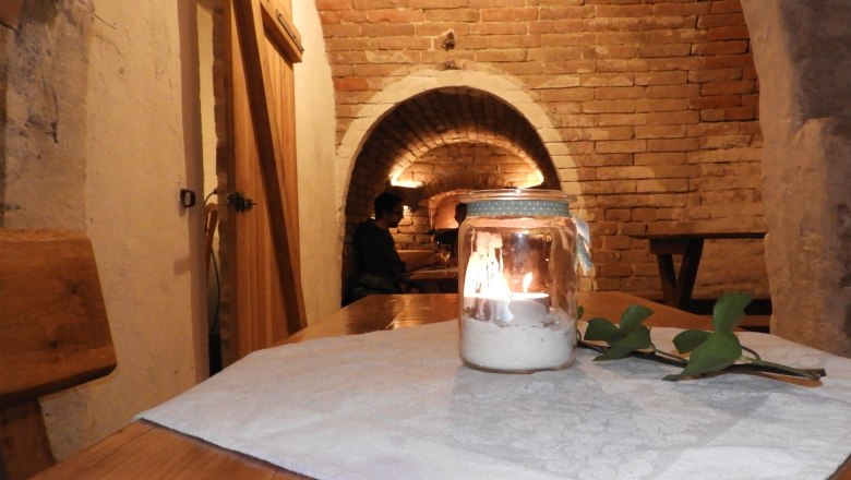 A cozy wine cellar with a candle on a table, brick walls and a vaulted ceiling.