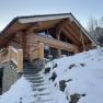 A wooden chalet covered in snow in winter, surrounded by trees.