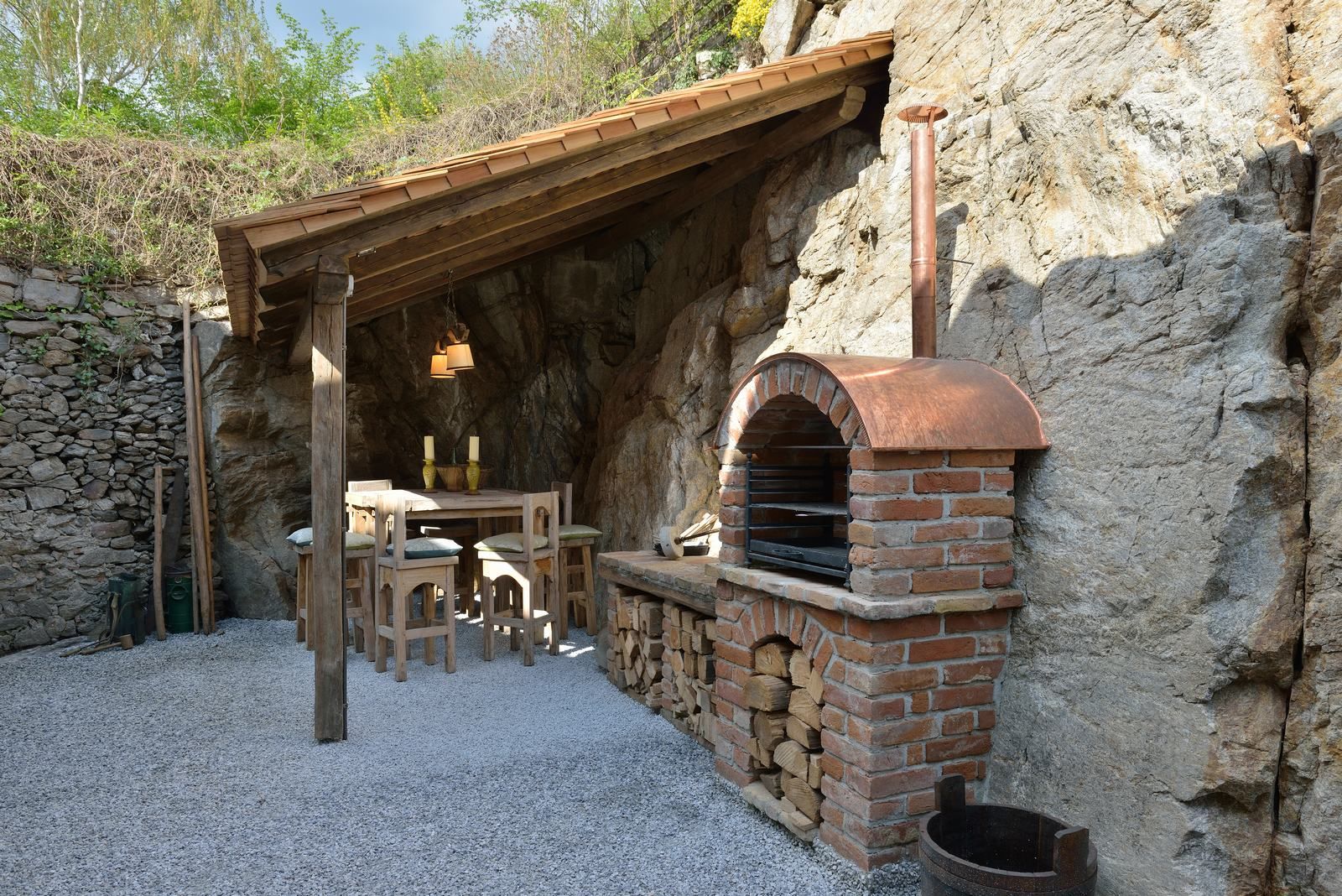 Rustic outdoor area with brick oven and wooden table under a wooden roof.