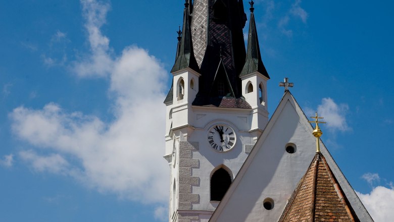Church tower with clock and pointed roof against a blue sky.