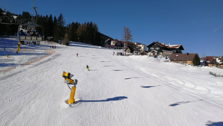 Skiers on a sunny slope in M&ouml;nichkirchen with chair lift and snow cannons.