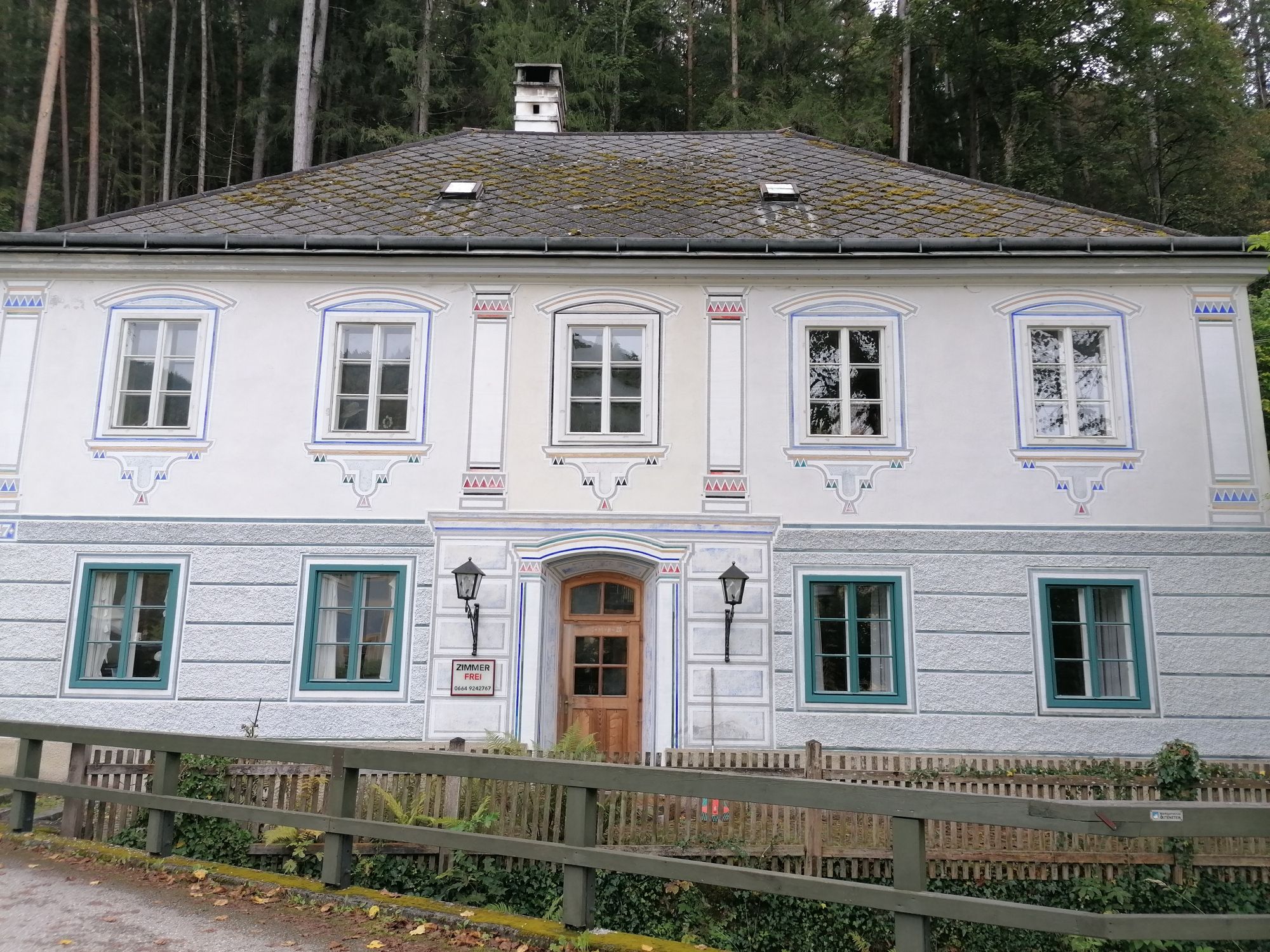 Historic building with ornate windows and wooden door, surrounded by forest.